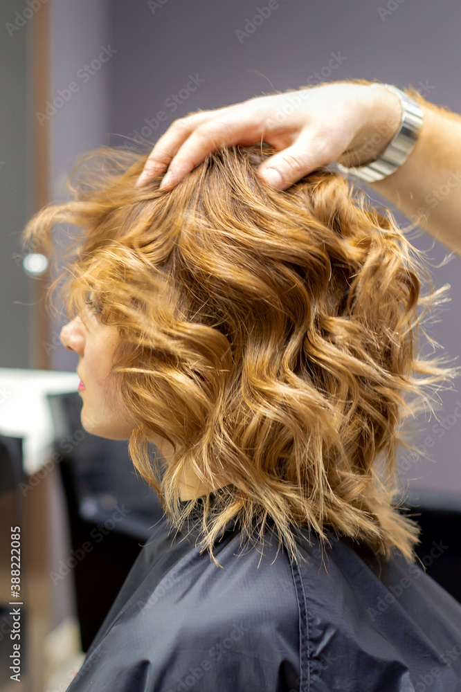 Side view of male hairdresser checks curly hairstyle of young caucasian woman in hair salon Side view of male hairdresser checks curly hairstyle of young caucasian woman in hair salon