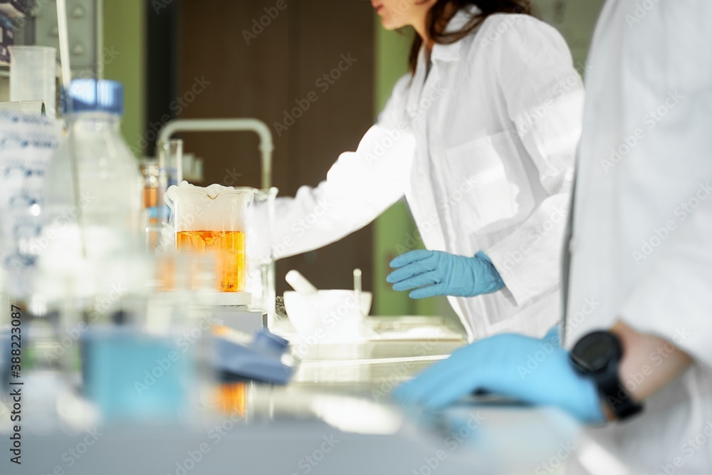 Fototapeta premium Glass beaker with liquid in laboratory background, Two laboratory technicians prepare the active substances