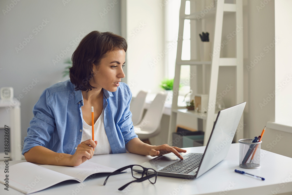 Woman sitting with laptop and notebook, watching online lesson or videocall and making notes Woman sitting with laptop and notebook, watching online lesson or videocall and making notes