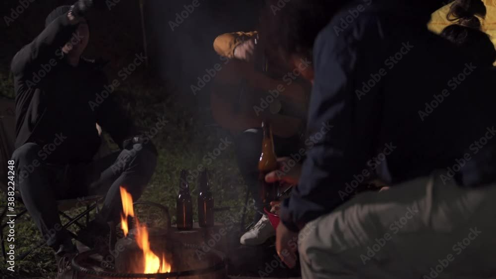Group of Asian man and woman sitting by campfire enjoy outdoor lifestyle party in forest at night. Happy friends having fun in camping trip with drinking beer, eating grilled bbq and singing together. Group of Asian man and woman sitting by campfire enjoy outdoor lifestyle party in forest at night. Happy friends having fun in camping trip with drinking beer, eating grilled bbq and singing together.