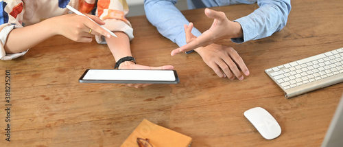 Cropped shot of business colleagues using tablet with empty screen for discussing business projects on wooden table.