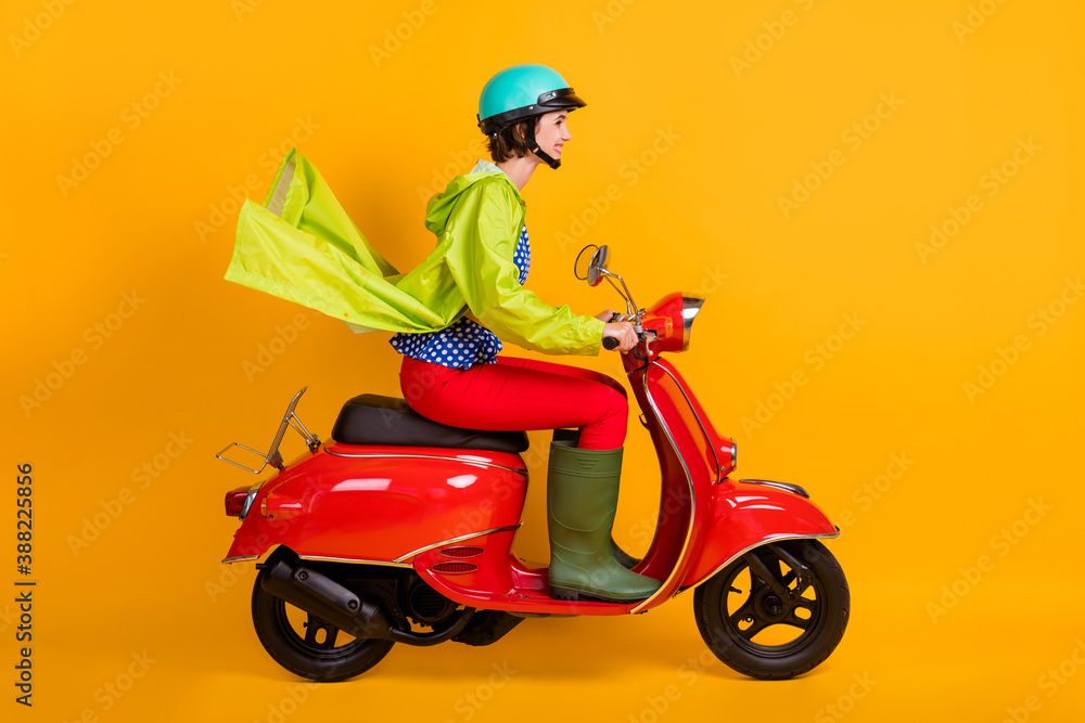 Full length photo portrait profile of woman on scooter isolated on bright yellow colored background Full length photo portrait profile of woman on scooter isolated on bright yellow colored background