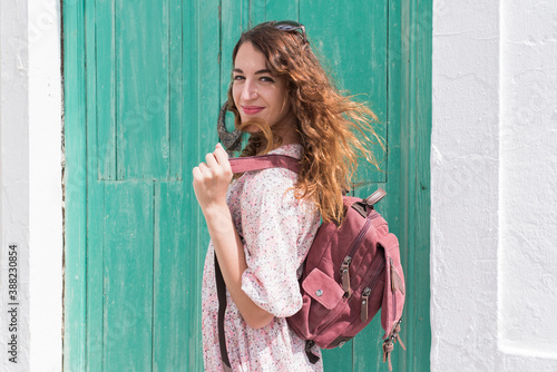 Young girl posing in front of a green door carrying a backpack with her.