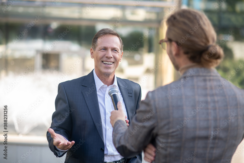 Smiling male speaking into microphone, answering long-haired journalist questions