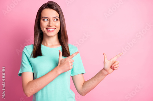 Photo portrait of pretty girl pointing with fingers looking on blank space smiling isolated on pastel pink color background