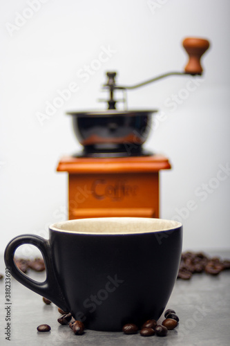 A black coffee mug with coffee beans dropped next to a coffee grinder backdrop.