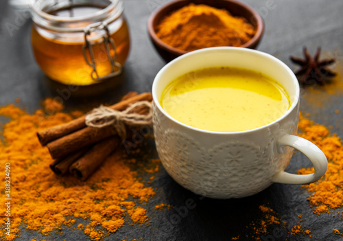 Yellow turmeric latte drink. Golden milk with cinnamon, turmeric, ginger and honey over black concrete background.