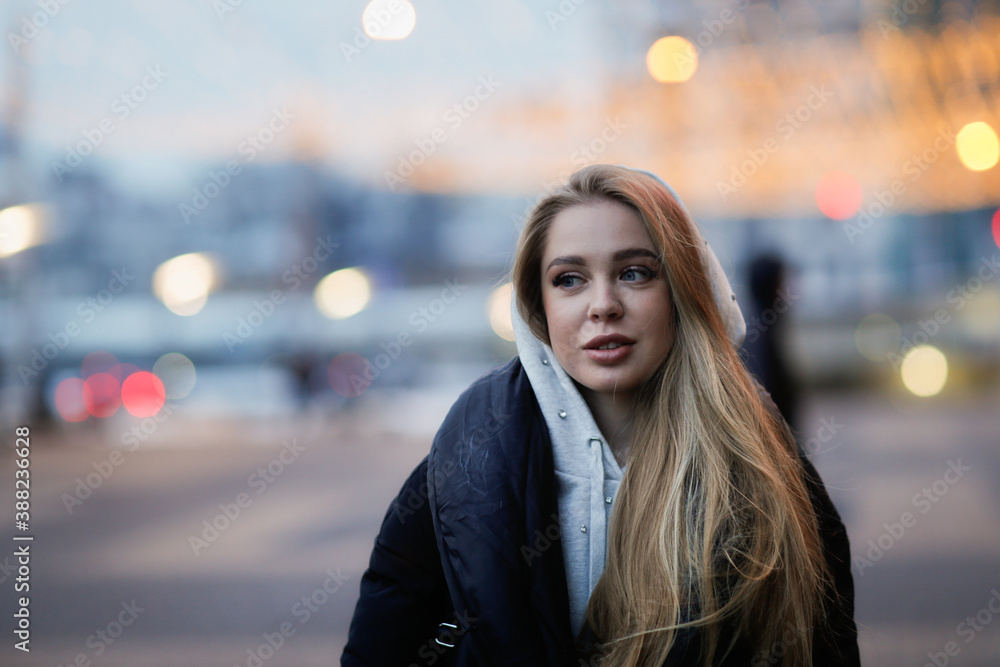 Fototapeta premium Caucasian girl woman in a long down coat in the city with a phone, the concept of safety and life in the city, communication
