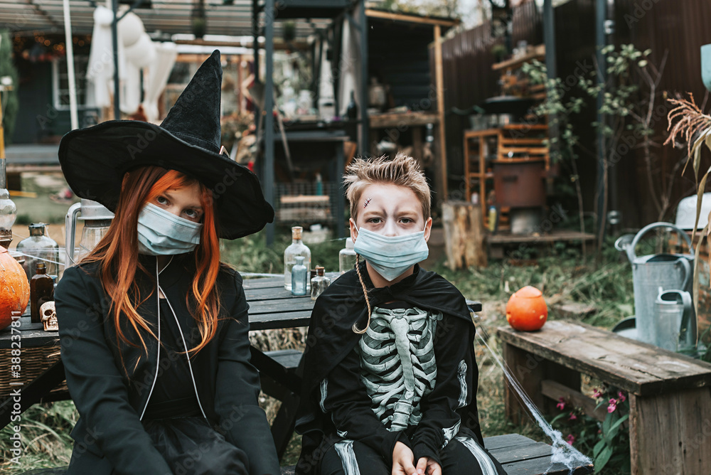 a boy in a skeleton costume and a girl in a witch costume wearing a protective face mask at a Halloween party in a new reality due to the covid pandemic