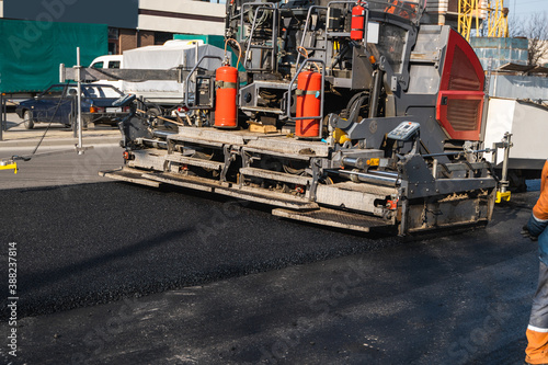 Industrial asphalt paver machine laying fresh asphalt on road construction site on the street. A Paver finisher placing a layer of a new hot asphalt on the roadway on a construction site. Repairing.