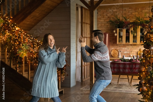 Overjoyed young Caucasian couple dance in decorated house celebrate New Year winter holidays together. Smiling happy man and woman have fun enjoy Christmas family celebration in own house.