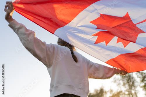 The flag of Canada in the hands of a person. Canadian symbol against the backdrop of a beautiful sunset. Pride and independence
