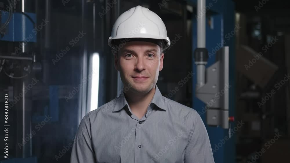 An engineer in a white helmet looks down, rices head and smiles An engineer in a white helmet looks down, rices head and smiles