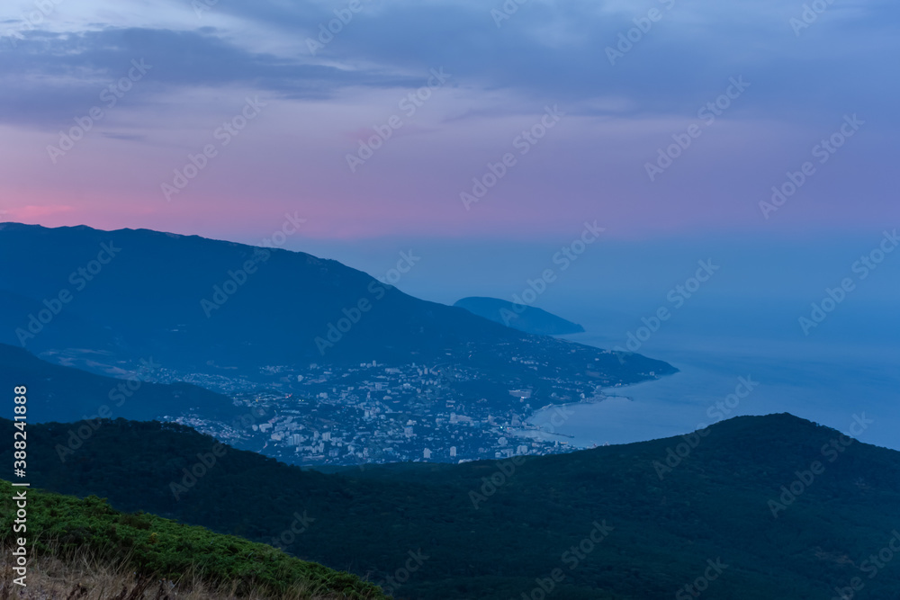 Fototapeta premium Fantastically beautiful sunset over Yalta from AI-Petri mountain. Autumn mountain landscape. Blue and pink shades of clouds. A popular tourist destination. Cloudy evening post-sunset landscape.