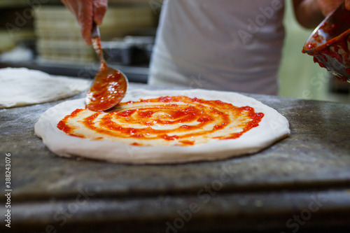 Pizzaiolo mentre stende il sugo di pomodoro su una pizza napoletana 