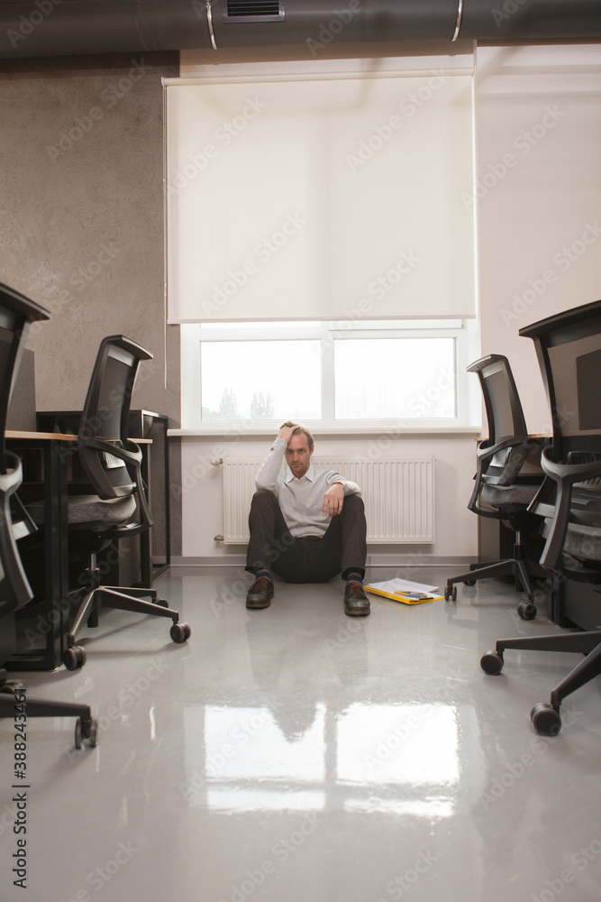 Vertical shot of a mature male office worker sitting alone on the floor, looking stressed and depressed