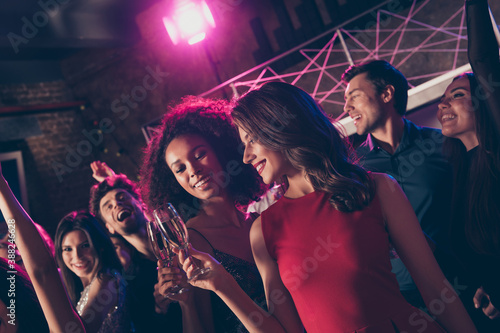 Photo portrait of two girls clinking champagne glasses with other people at big party in background