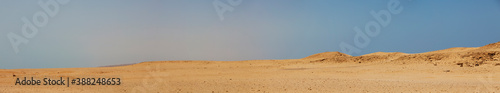 Super wide panorama of a desert landscape with a hazy blue sky.