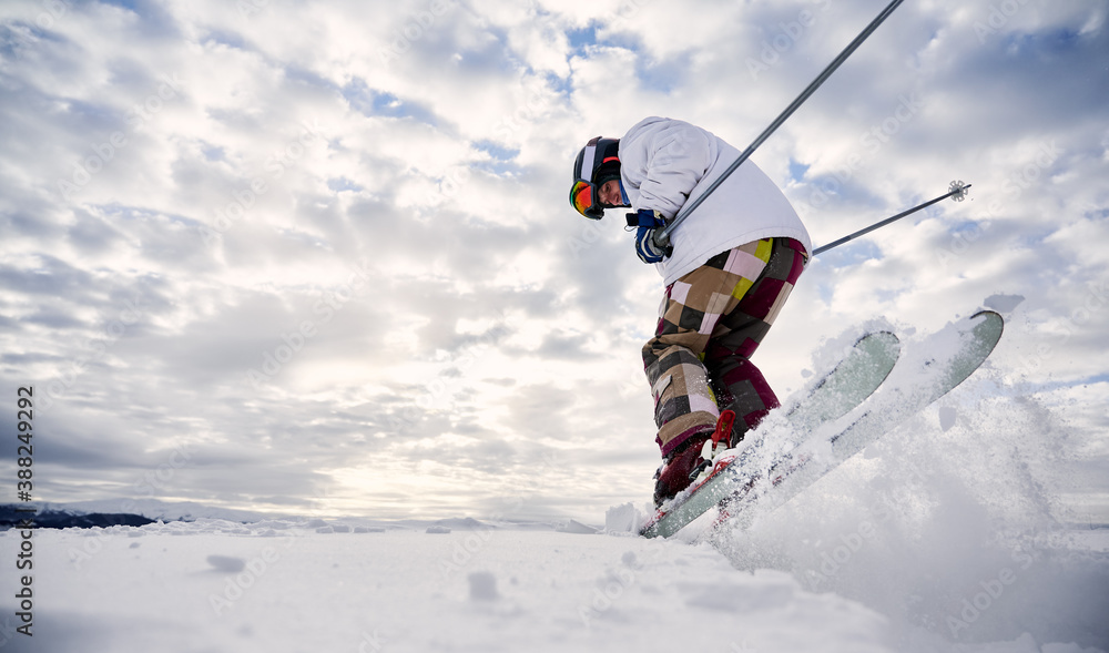 Low angle view snapshot of skier's legs wearing colorful ski pants making a jump up on white snowy surface against beautiful cloudy sky. Copy space. Concept of winter sport activities. Low angle view snapshot of skier's legs wearing colorful ski pants making a jump up on white snowy surface against beautiful cloudy sky. Copy space. Concept of winter sport activities.