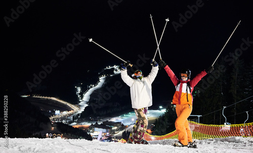Fotografie Cheerful male and female skiers in winter jackets and helmets raising ski poles