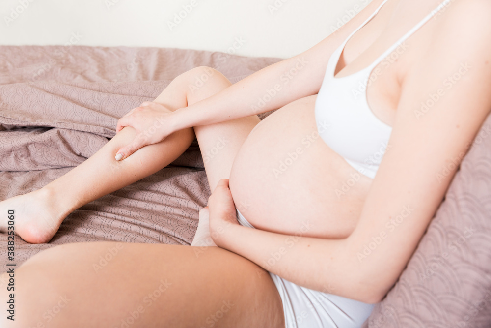 Pretty pregnant woman hands massaging leg sitting on bed Pretty pregnant woman hands massaging leg sitting on bed