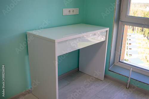 Wooden cosmetic beauti table with glass and drawer. White table in the corner of the room near big window. photo