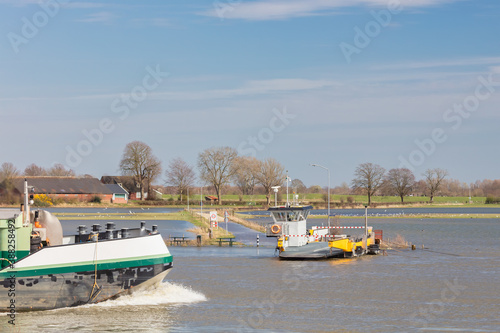 Ferry on the Dutch flooded river IJssel in the province of Gelderland with ship passing by