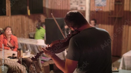 People in small cafe in mountains sit at rtables and listen to violinnist playing violin. photo