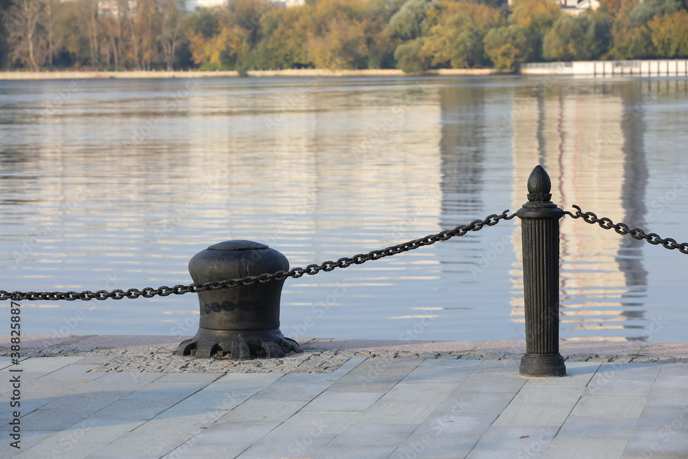 Obraz premium Iron fence near the water.The metal parapet on the embankment of the river.Black chain on a post. Decorative barrier on the sidewalk at the edge of the coastline beautiful view with reflection