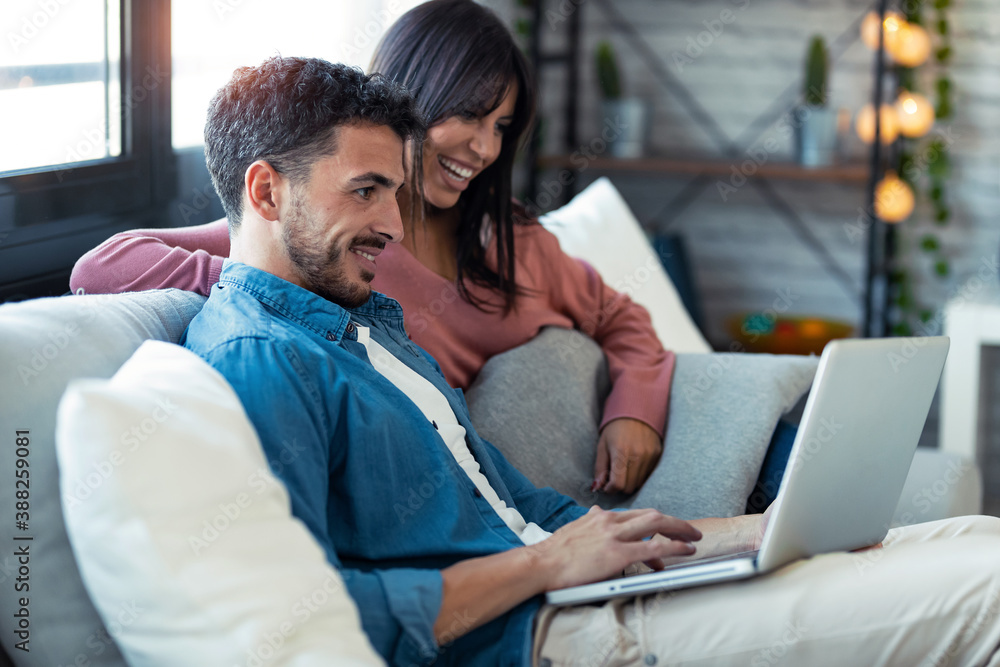 Happy beautiful couple using computer while sitting on the couch at home. Happy beautiful couple using computer while sitting on the couch at home.