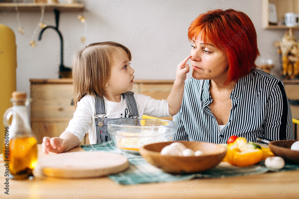 Cook together at home. Red-haired grandmother and little granddaughter cook pizza in a cozy home. Have fun in the kitchen