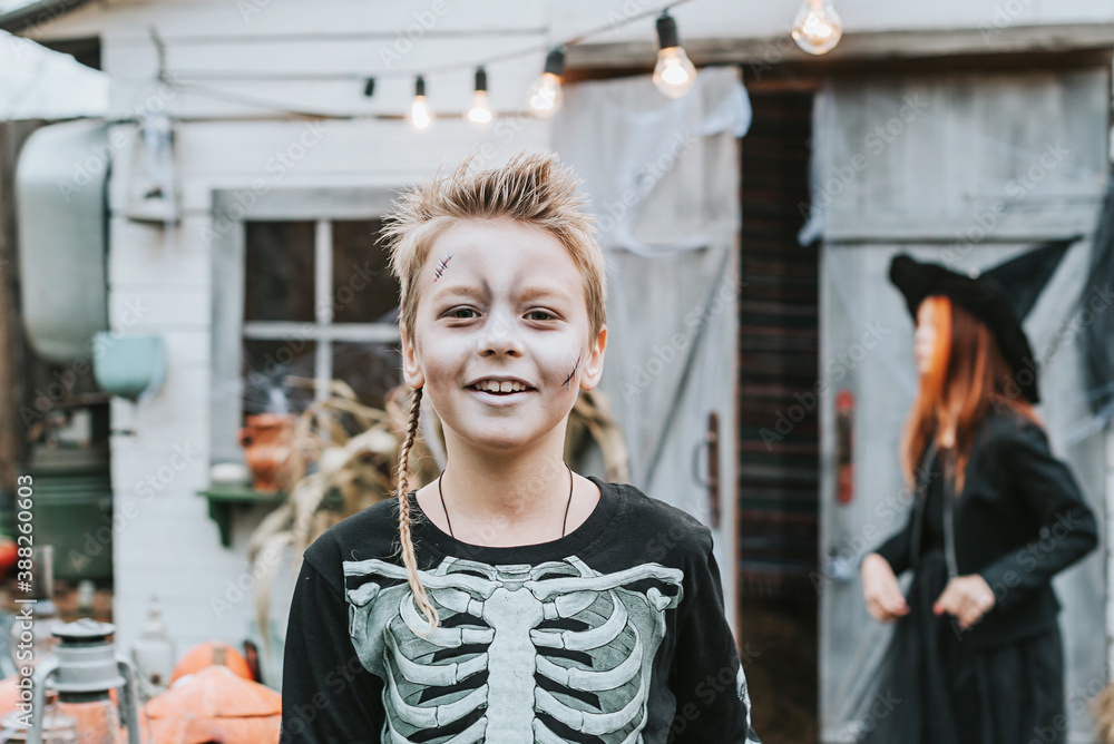 a boy in a skeleton costume with a painted face on the porch of a house decorated to celebrate a Halloween party