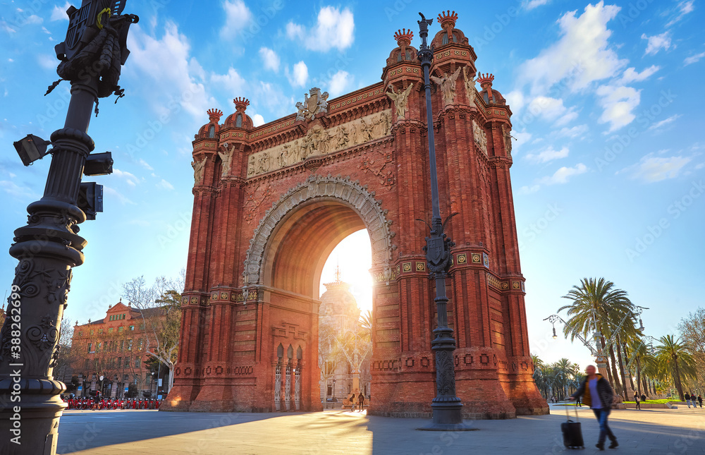 Obraz premium Sunrise at Triumphal Arch in Barcelona, Catalonia, Spain. Arc de Triomf at boulevard street. Alley with tropical palm trees. Early morning landscape with shadows and blue sky with clouds. Famous.