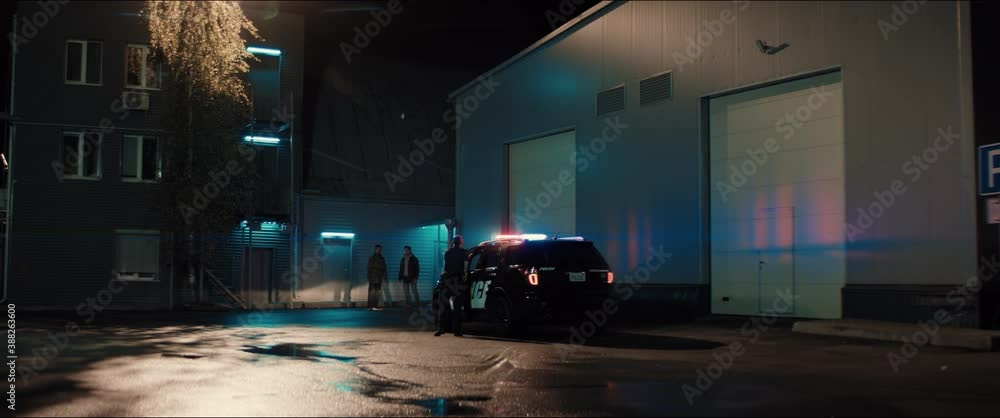 WIDE Police officer exiting a car and approaching two multi-ethnic males suspects near industrial buildings at night. Shot on RED cinema camera with 2x Anamorphic lens WIDE Police officer exiting a car and approaching two multi-ethnic males suspects near industrial buildings at night. Shot on RED cinema camera with 2x Anamorphic lens