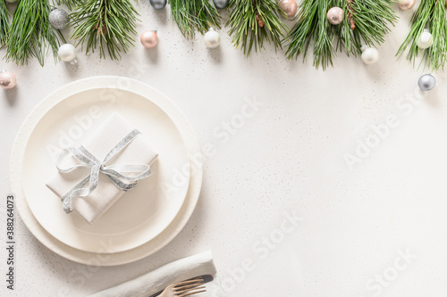 Christmas table setting with white gift and silver decorations on white.
