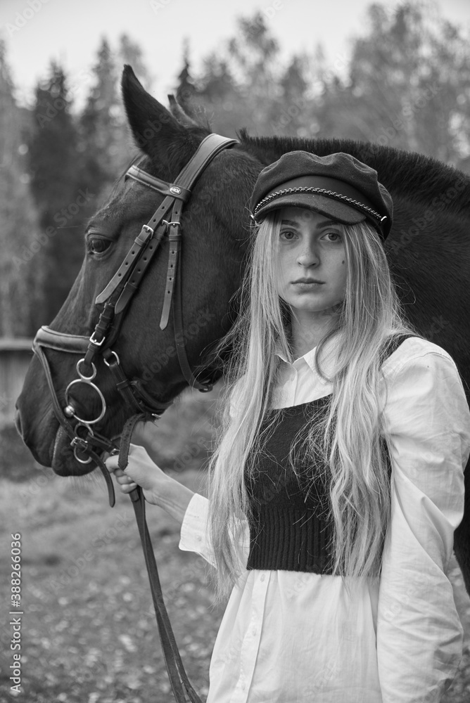 Obraz premium Large portrait of a girl with blonde hair and a Bay horse on the background of an autumn forest.