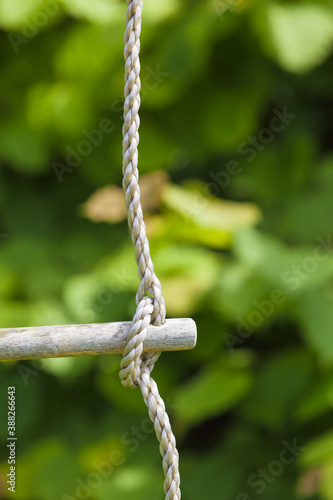 Outdoor Rope Concept / Detail of corded ladder - knot in rope at wooden step stick - on green tranquil garden plant background (copy space)