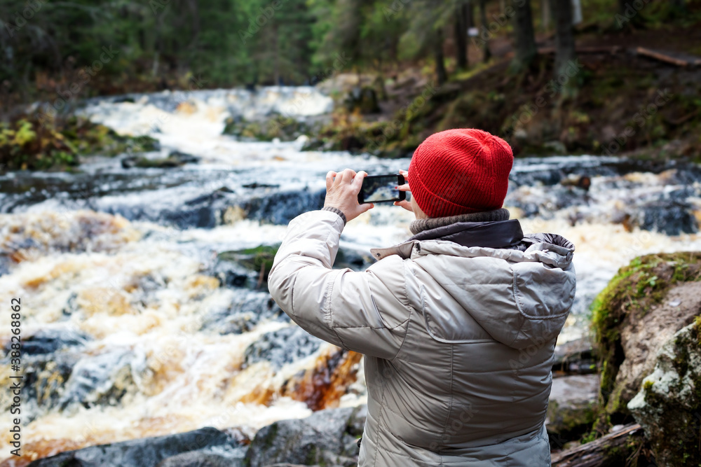 Traveller makes photo on smartphone in forest with karelian waterfalls. Traveller makes photo on smartphone in forest with karelian waterfalls.