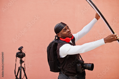 Young professional african american videographer holding professional camera with pro equipment. Afro cameraman wearing black duraq making a videos. photo