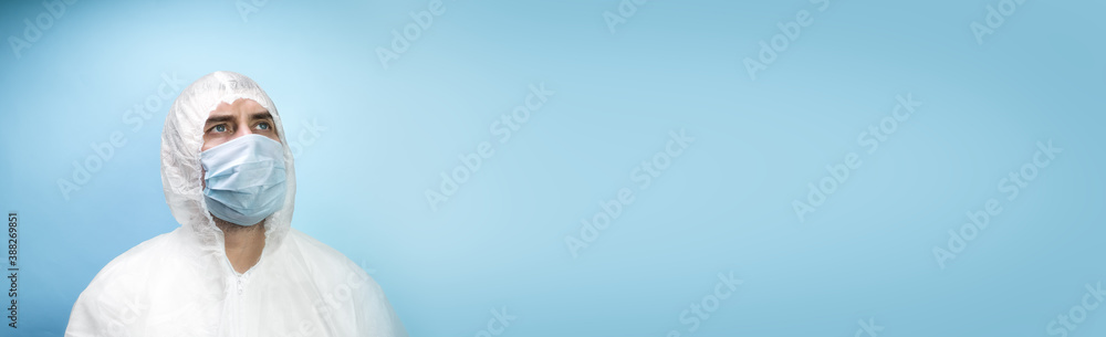 Man in medical mask wearing protective uniform on blue background. Covid 19 quarantine concept Man in medical mask wearing protective uniform on blue background. Covid 19 quarantine concept