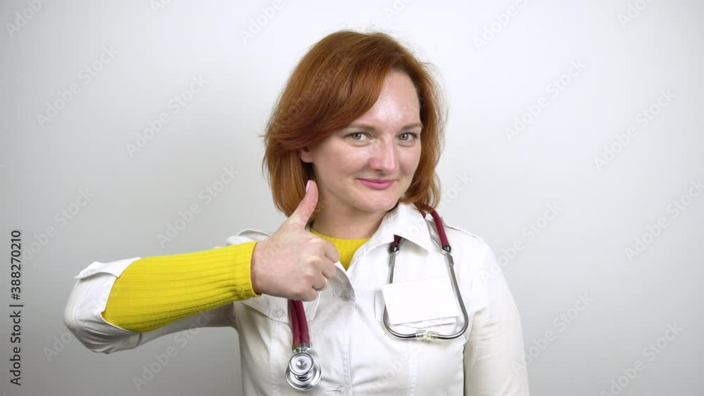 Young female doctor smiling and showing thumb up. Portrait of a woman in a medical gown with a stethoscope around her neck. White background. 4k Young female doctor smiling and showing thumb up. Portrait of a woman in a medical gown with a stethoscope around her neck. White background. 4k