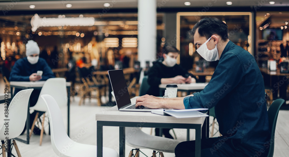 image of people in protective masks using laptops in a food court. image of people in protective masks using laptops in a food court.
