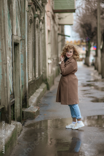 A beautiful young woman walks down the street with wet asphalt. The girl turns back © Kiryakova Anna