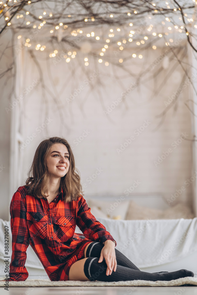 Pretty brunette girl sitting on the floor in red shirt and warm socks with christmas tree behind. Pretty brunette girl sitting on the floor in red shirt and warm socks with christmas tree behind.