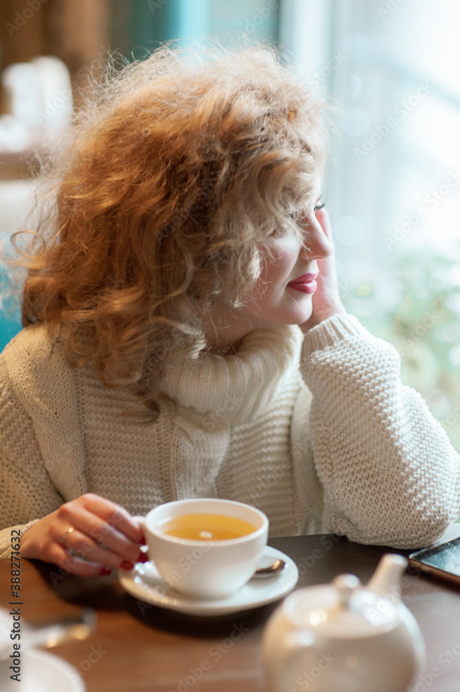 A beautiful girl sits in a cafe with a cup of tea and looks out the window. Inside A beautiful girl sits in a cafe with a cup of tea and looks out the window. Inside