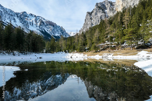 Winter landscape of Austrian Alps with Green Lake in the middle. Powder snow covering the mountains and ground. Soft reflections of Alps in calm lake's water. Winter wonderland. Serenity and calmness