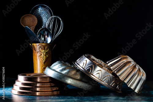 Arrangement of bundt cake pans against a dark background with a vintage tin of utensils in soft focus in behind. photo