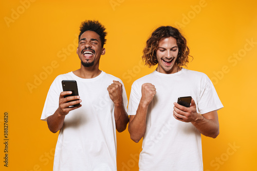Excited multicultural guys using smartphones and making winner gesture photo