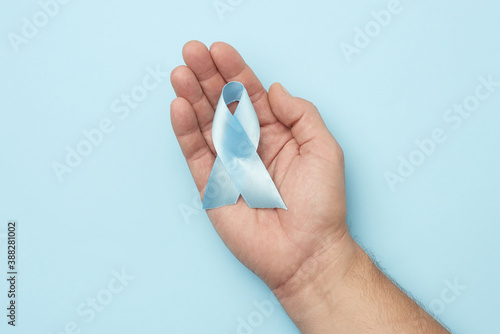 male hand holds blue silk ribbon in the shape of a loop on a blue background