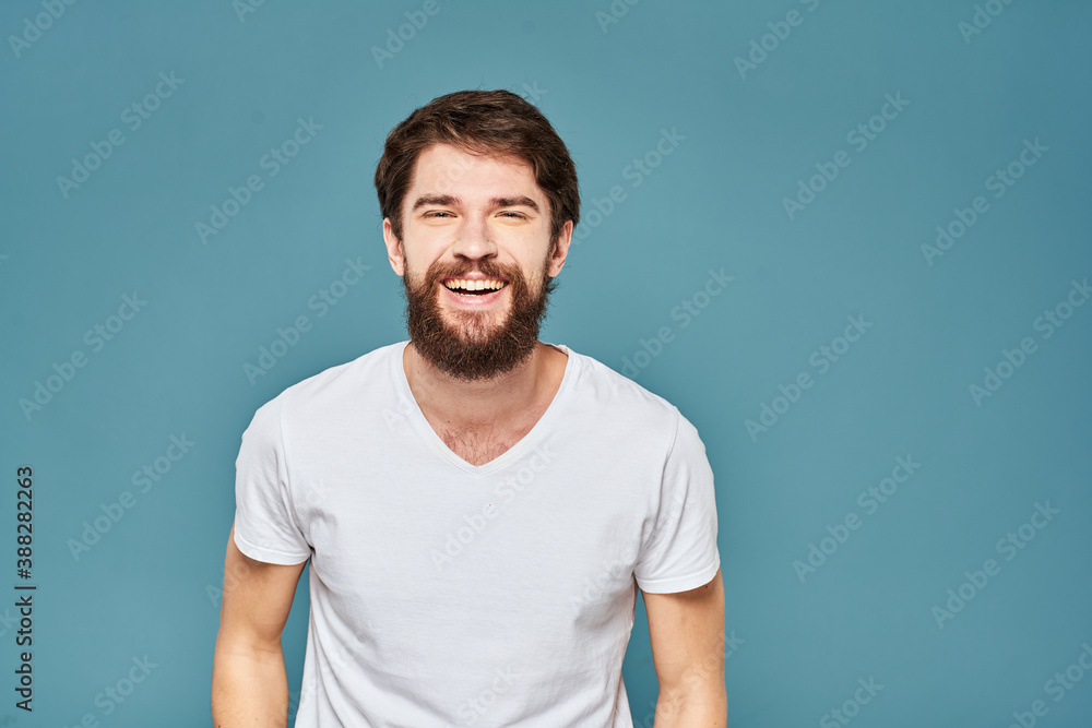 A bearded man in a white T-shirt gestures with his hands emotions blue background A bearded man in a white T-shirt gestures with his hands emotions blue background